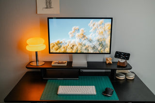 Dark wood desk shelf with a 27-inch display, walnut MagSafe stand, and orange glass lamp on a minimalist workspace.