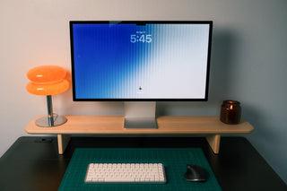 Maple desk shelf holding a 27-inch display and orange glass lamp, with keyboard and mouse on a green cutting mat below.