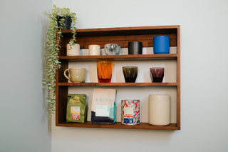 Tilde Made Monolith Wall Shelf in walnut, mounted on a white wall and styled with mugs, ceramics, coffee bags, and a trailing plant across three solid hardwood tiers