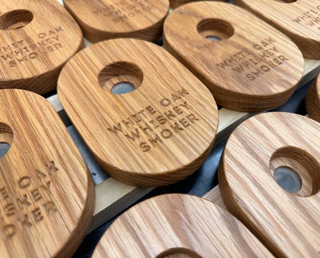 Close-up of stacked White Oak Whiskey Smoker lids showing the oak grain, engraved lettering and mesh smoke screen