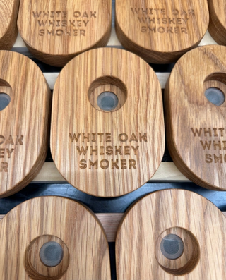 Overhead view of several handmade White Oak Whiskey Smoker lids arranged in rows, showing the burned-in logo engraving and center mesh smoke screen