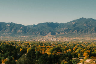 Landscape view of Colorado Springs with the Rocky Mountain Front Range behind the city skyline and fall-colored trees in the foreground.