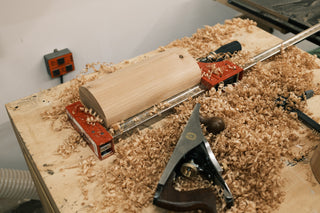 Workshop scene with a wood board clamped on a workbench during planing, surrounded by fresh wood shavings and a hand plane.