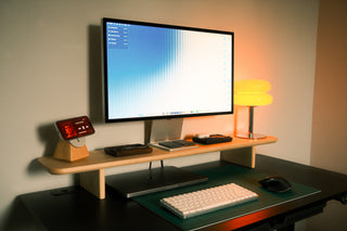 Wide-angle view of a maple Monolith Desk Shelf setup with monitor, MagSafe stand, yellow lamp, and keyboard on a dark standing desk.