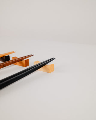 Black chopsticks resting on a maple chopstick rest, angled view