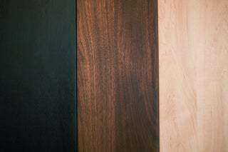 Three hardwood finish swatches side by side — ebonized black oak, walnut, and maple — for the Monolith Desk Shelf.