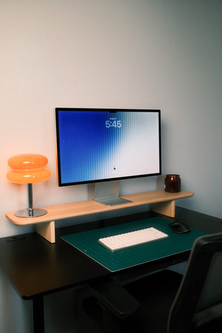 Home office with a maple Monolith Desk Shelf holding a monitor and an orange mushroom lamp, keyboard on green desk mat below.
