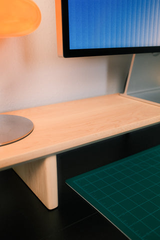 Wooden desk with a computer monitor and green cutting mat on a black floor.