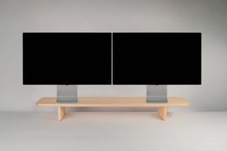 Wide maple Monolith Desk Shelf holding two monitors side by side — dual-monitor configuration on a white background.